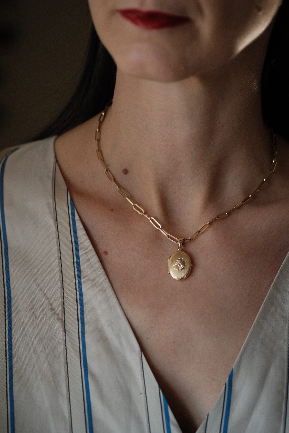 A 14K gold flower ocal locket with a gold paperclip chain on a neck