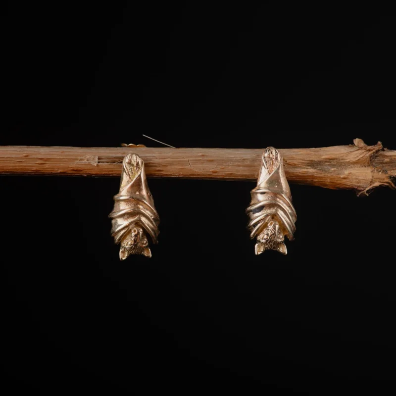 An image showing a pair of 14K gold bat stud earrings hanged from a tree branch