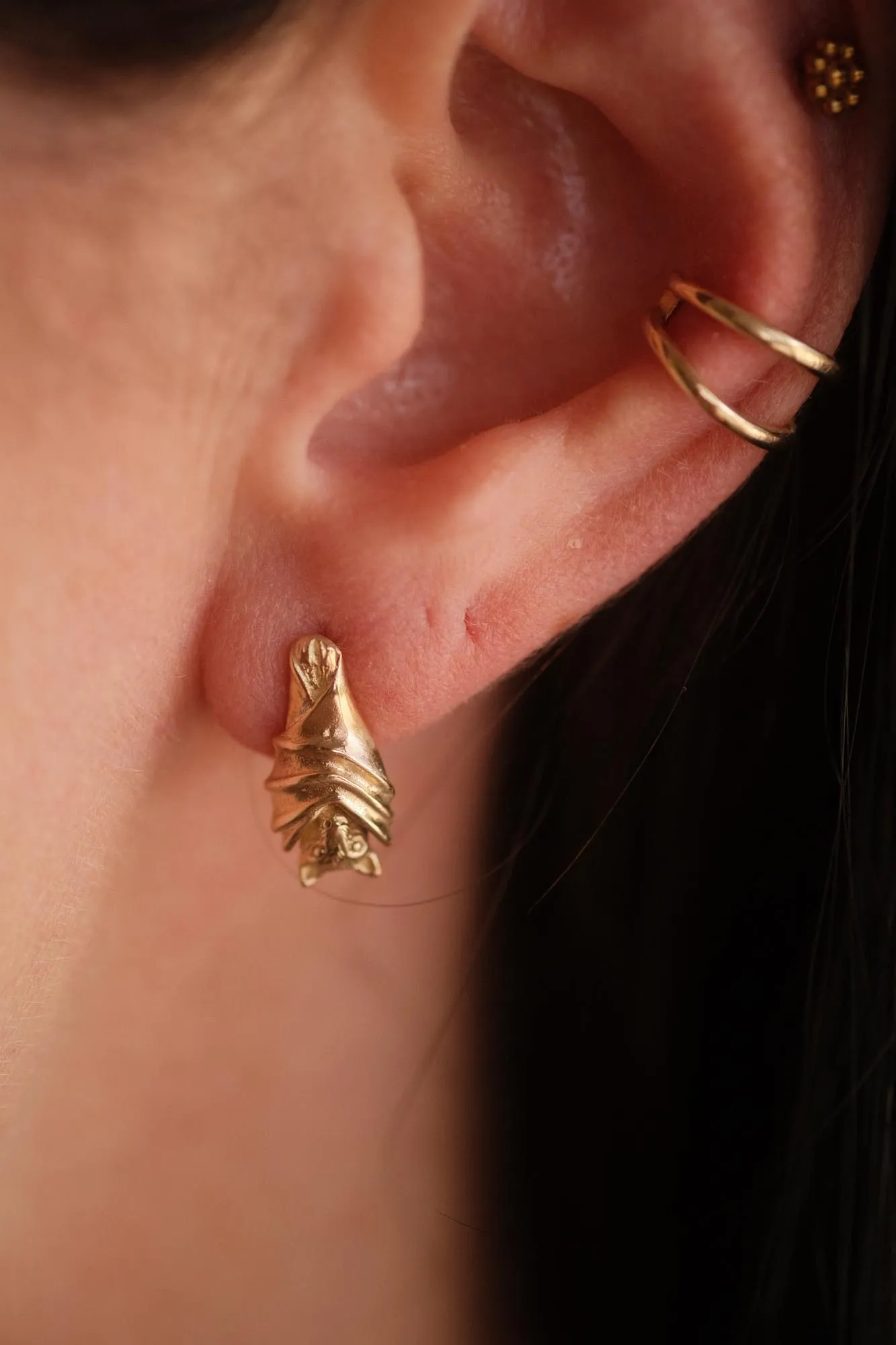 An image showing a pair of 14K gold bat stud earrings on an ear
