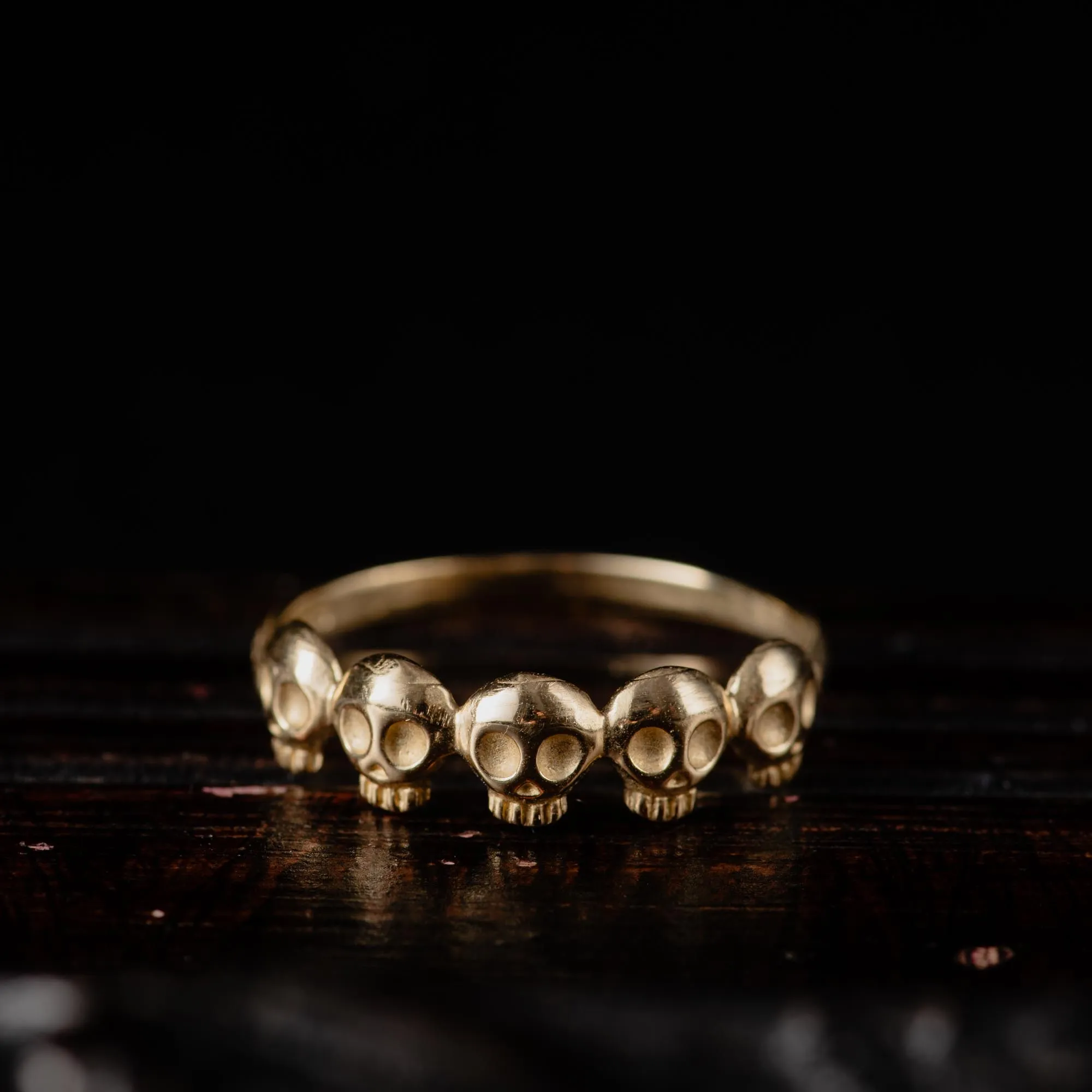 An image showing a 14K gold ring featuring 5 little skulls