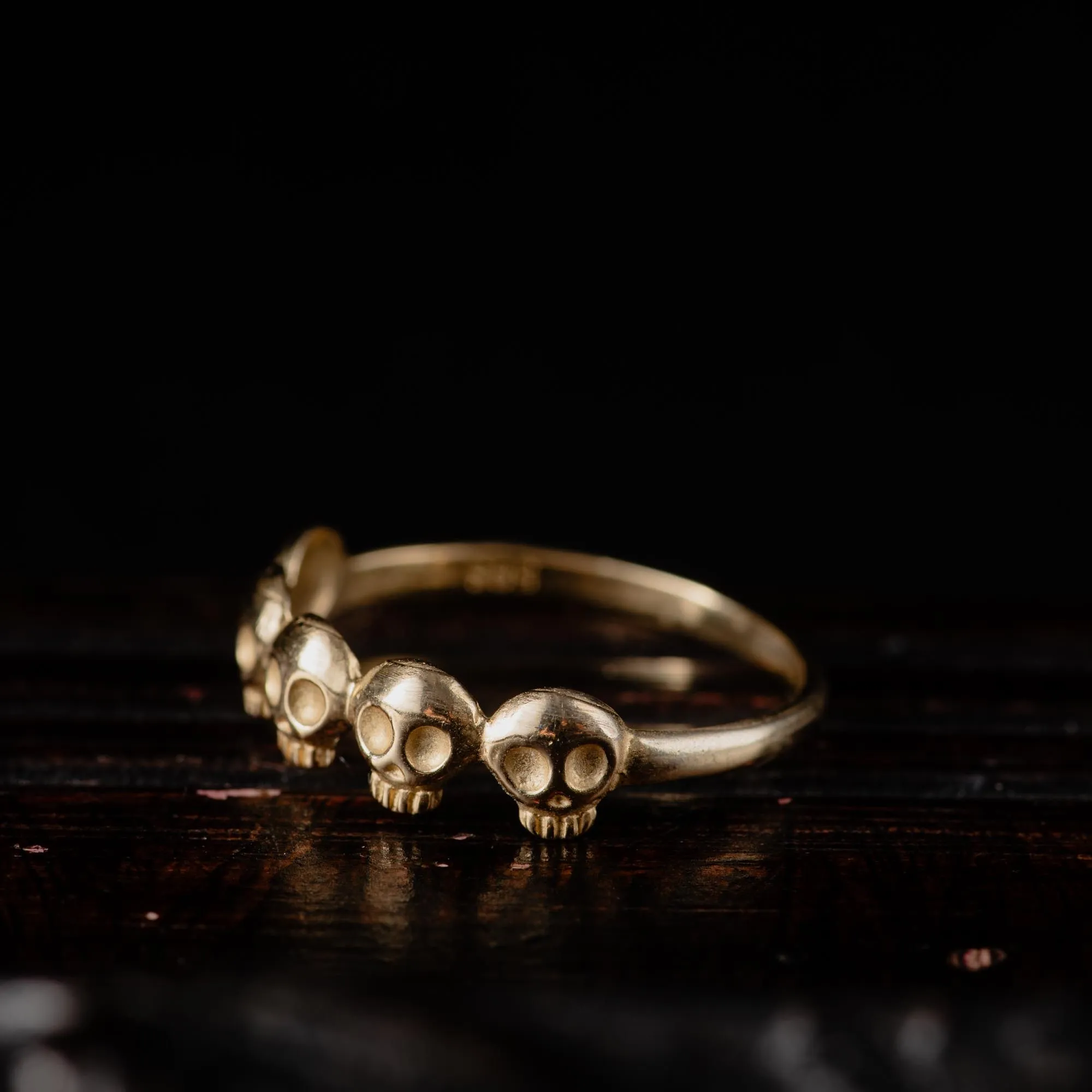 An image showing a 14K gold ring featuring 5 little skulls from the side