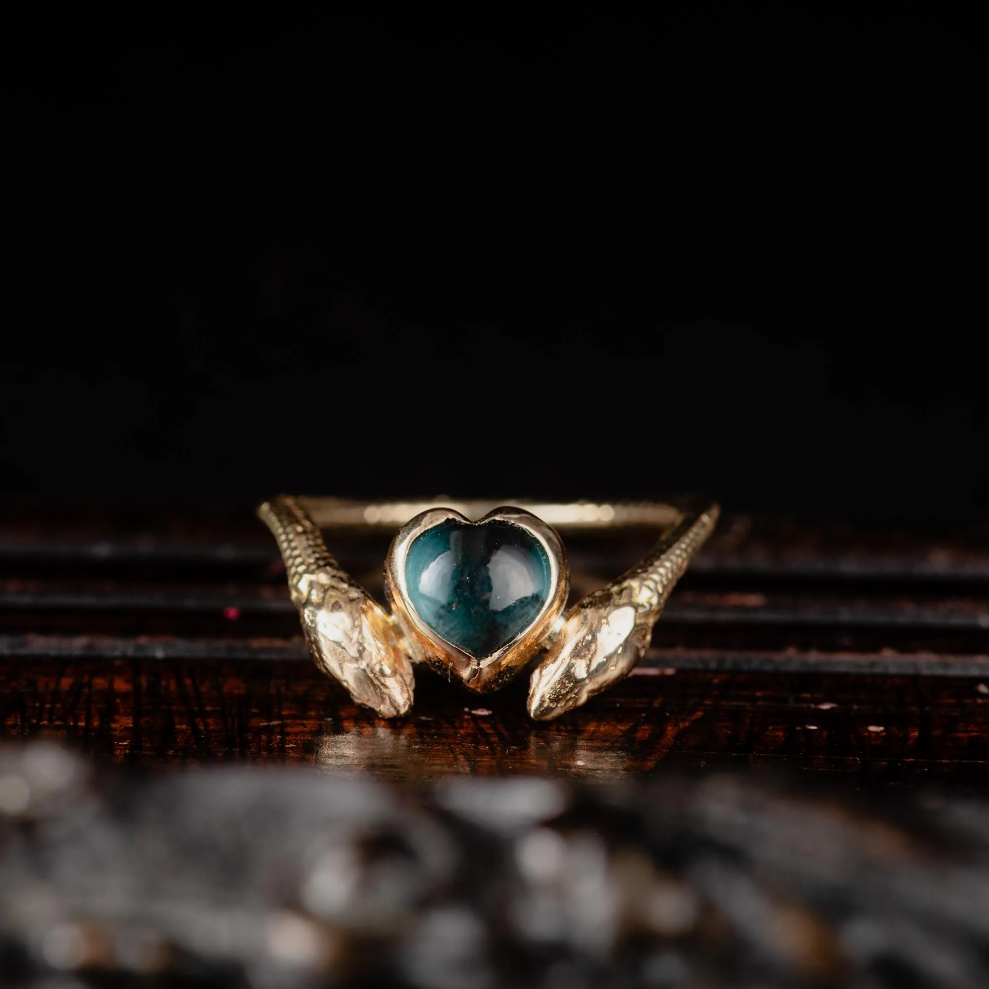 An image showing a 14K gold ring featuring a heart shaped london blue topaz and a snake in each side of the ring