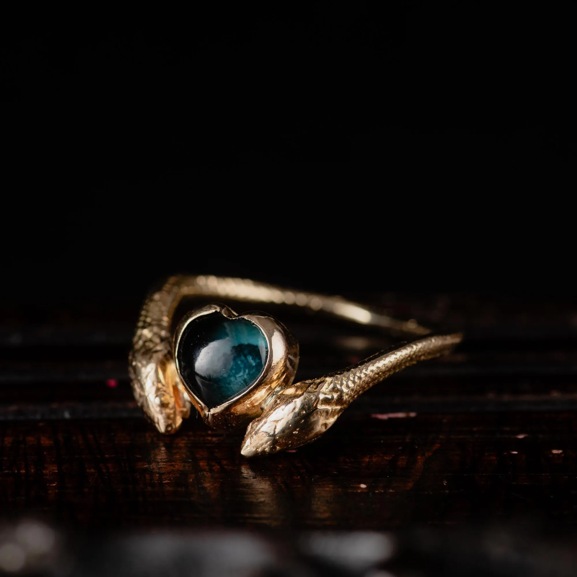 An image showing a 14K gold ring featuring a heart shaped london blue topaz and a snake in each side of the ring from the side