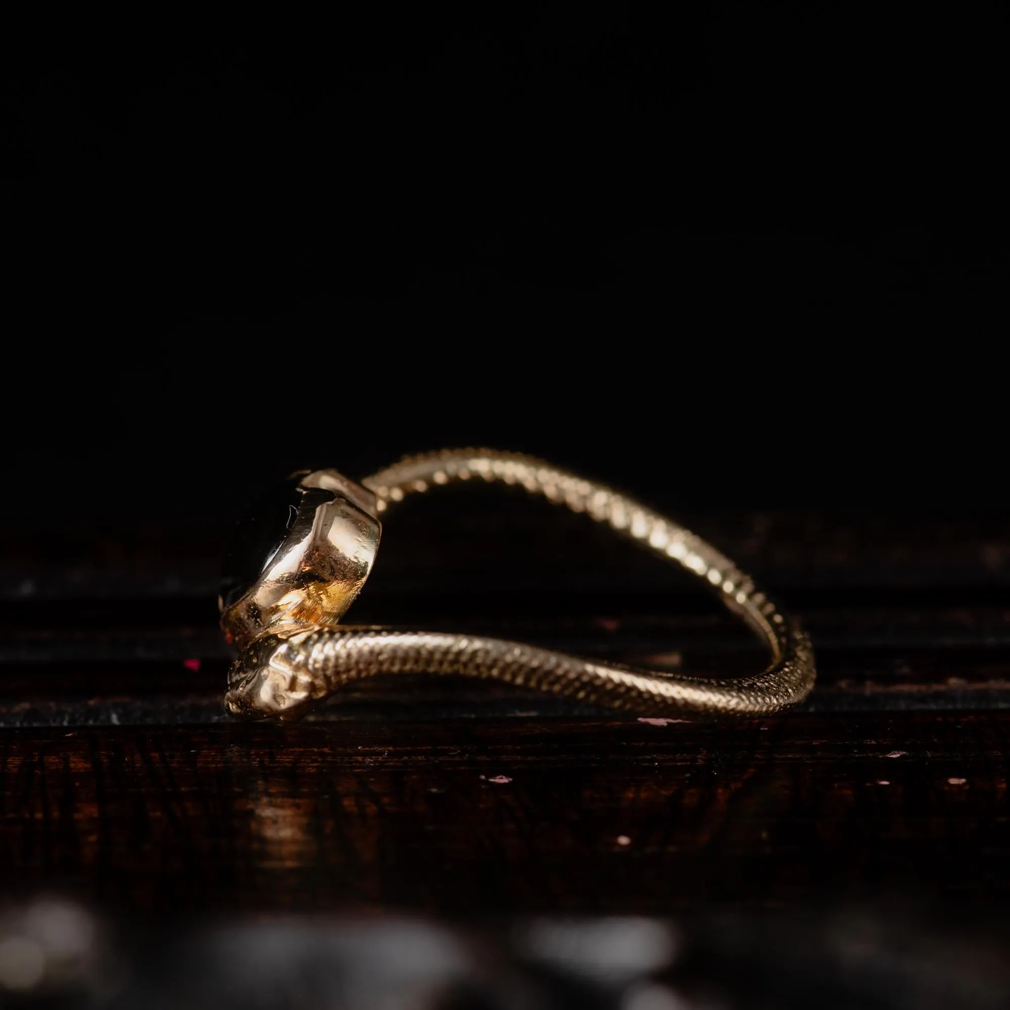 An image showing a 14K gold ring featuring a heart shaped london blue topaz and a snake in each side of the ring from the side