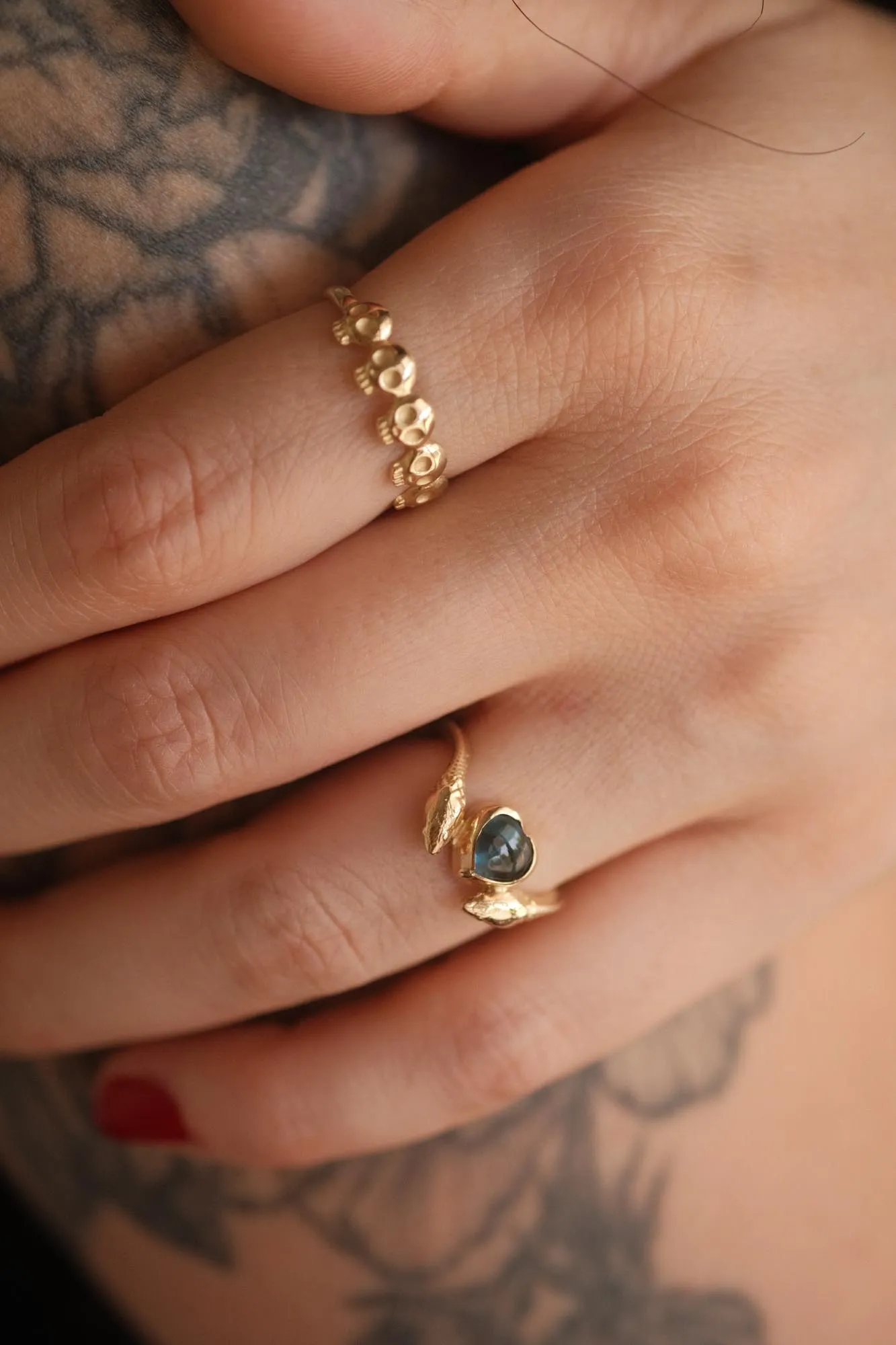 An image showing a 14K gold ring featuring a heart shaped london blue topaz and a snake in each side of the ring from the side on a finger