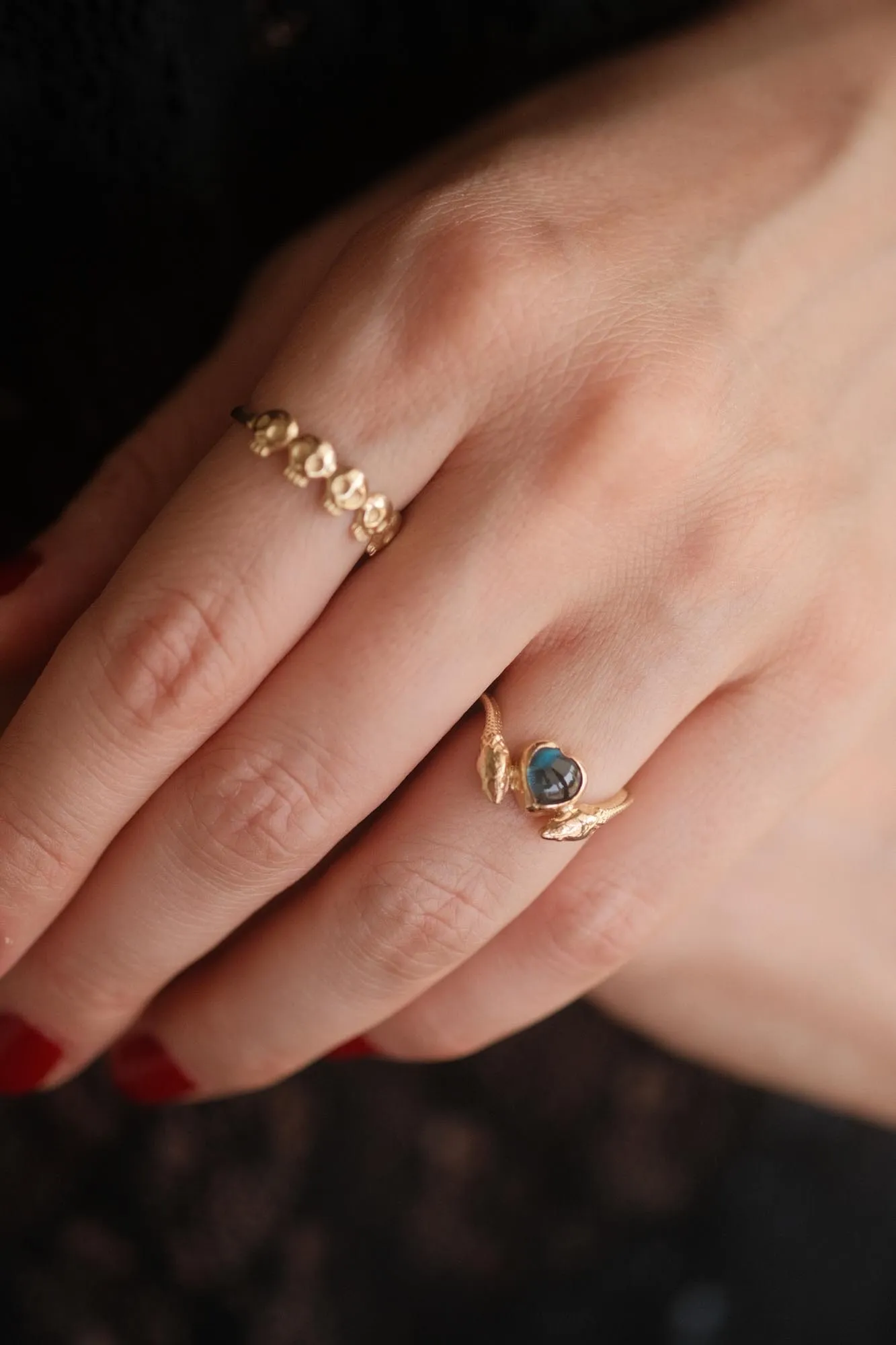 An image showing a 14K gold ring featuring a heart shaped london blue topaz and a snake in each side of the ring from the side on a finger