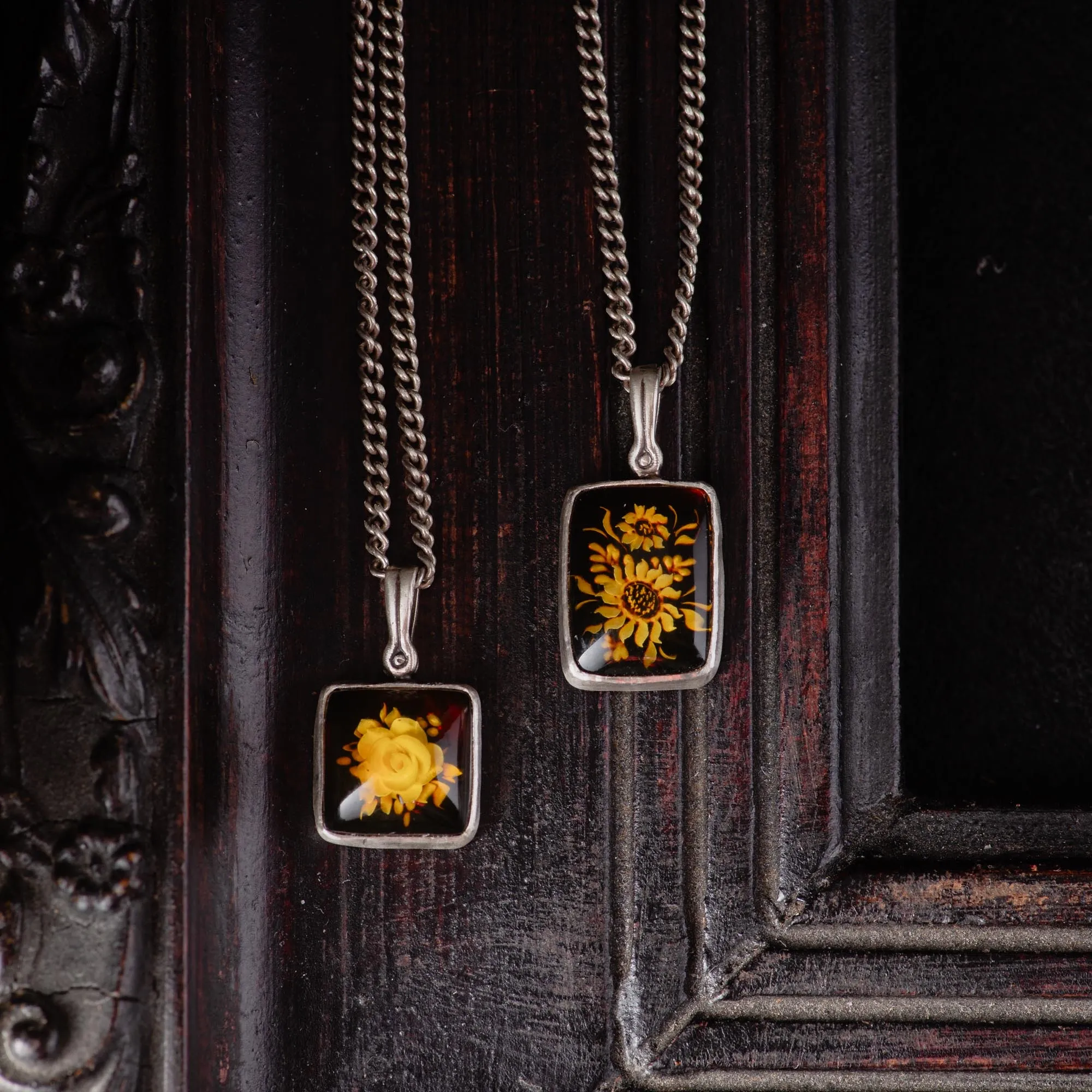 An image showing two sterling silver flower carved amber pendants