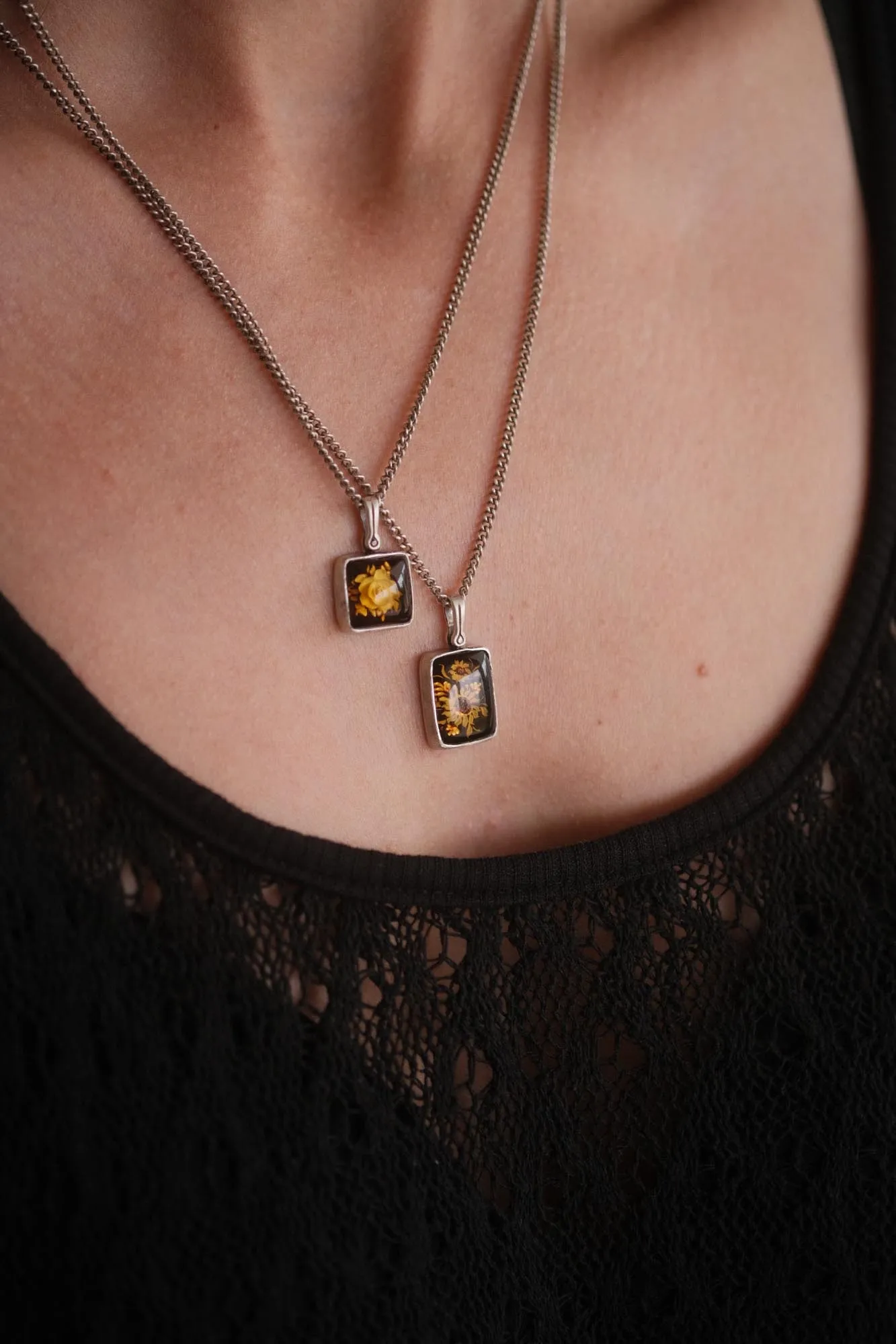 An image showing two sterling silver flower carved amber pendants worn on a model
