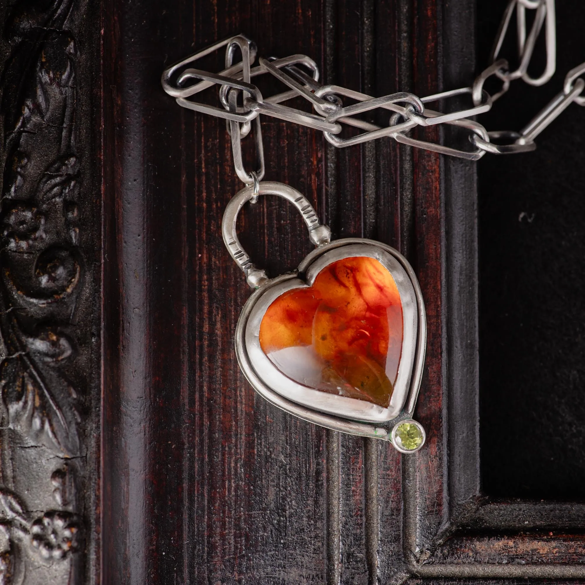 An image showing a glorious orange heart shaped amber sterling silver pendant with paperclip chain