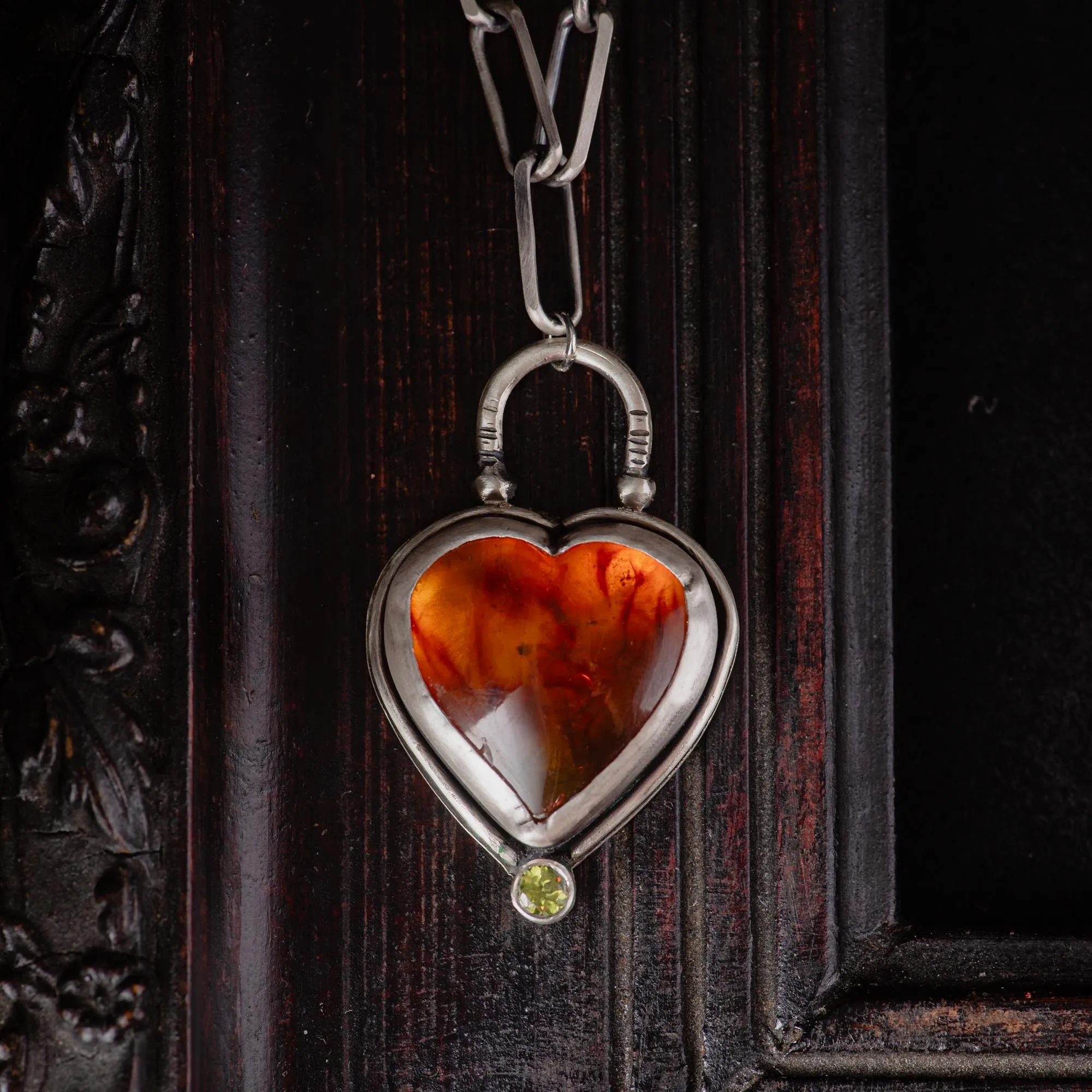 An image showing a glorious orange heart shaped amber sterling silver pendant with paperclip chain