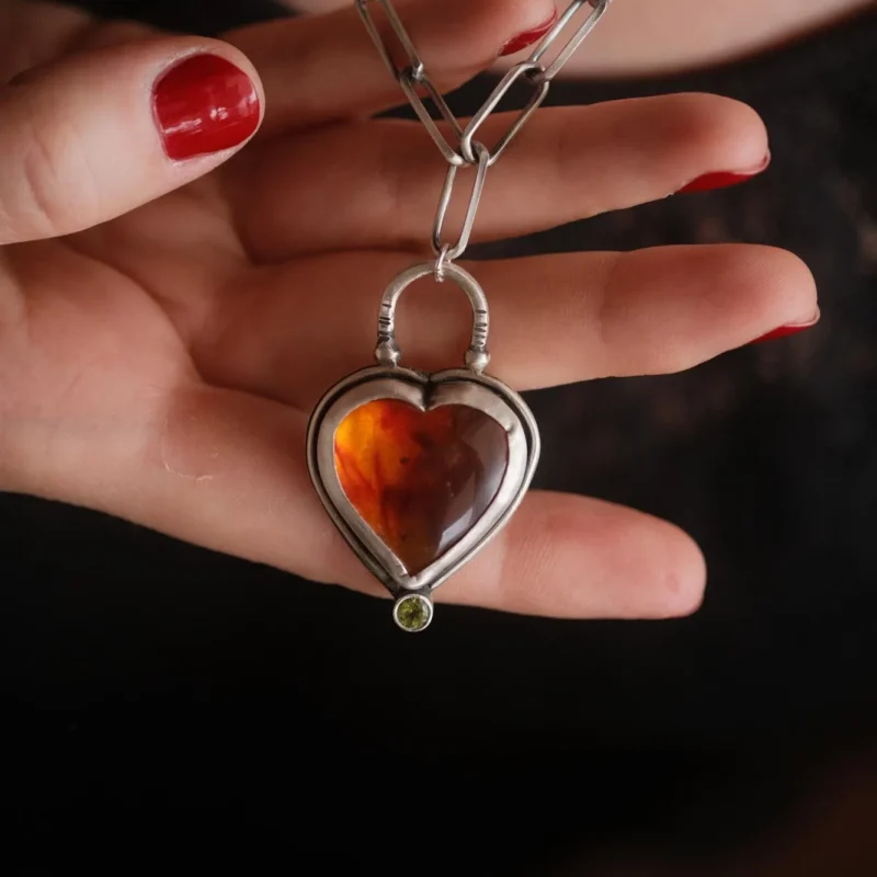 An image showing a glorious orange heart shaped amber sterling silver pendant with paperclip chain worn on a model