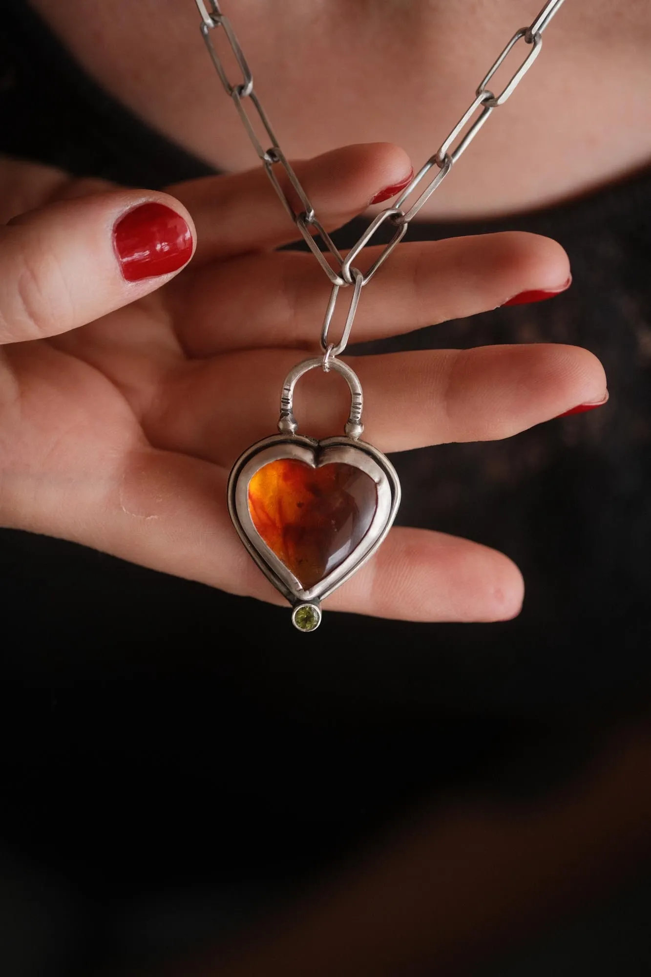 An image showing a glorious orange heart shaped amber sterling silver pendant with paperclip chain worn on a model