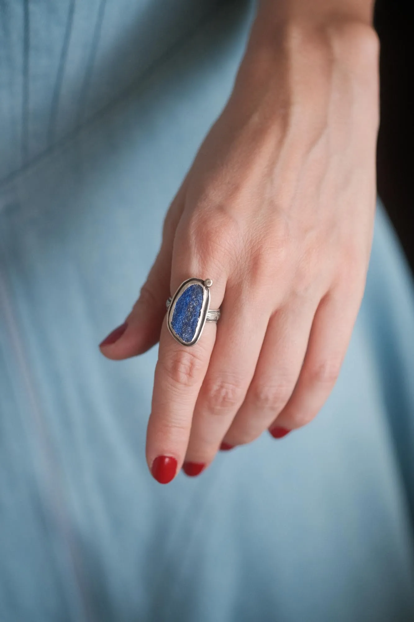 An image showing a raw blue azurite sterling silver ring with floral band on a finger
