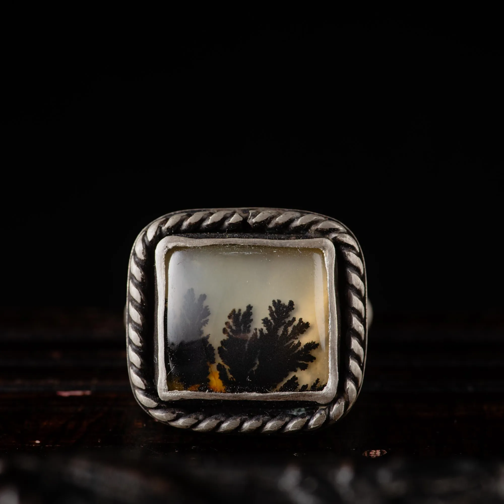 An image showing a rectangular dendritic agate gemstone with twisted border on a sterling silver ring