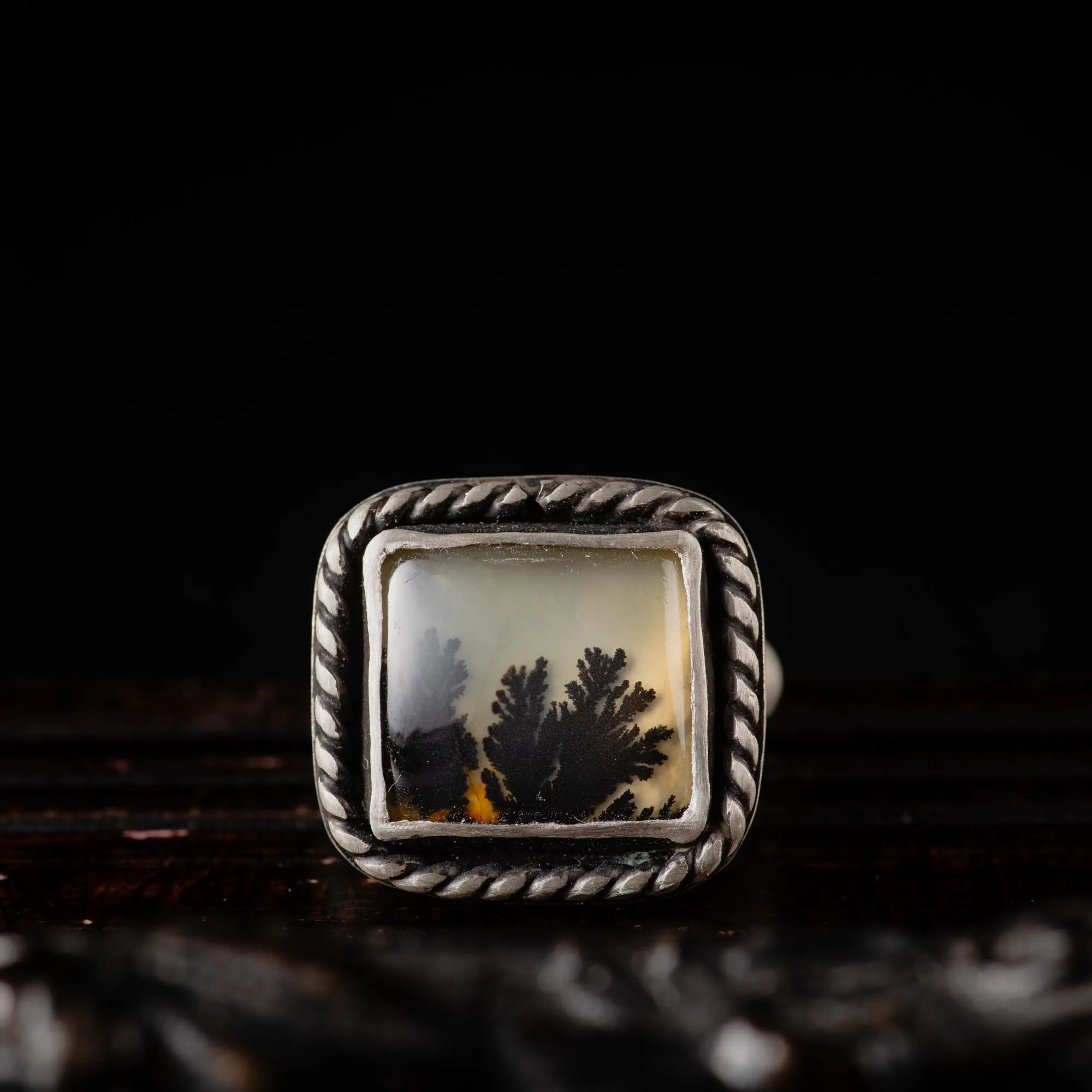 An image showing a rectangular dendritic agate gemstone with twisted border on a sterling silver ring