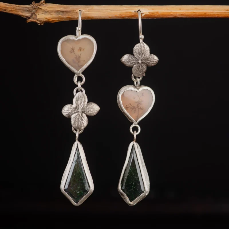 An image showing a sterling silver pair of earrings featuring dendritic agate in heart shaped and moss agate in kite shaped