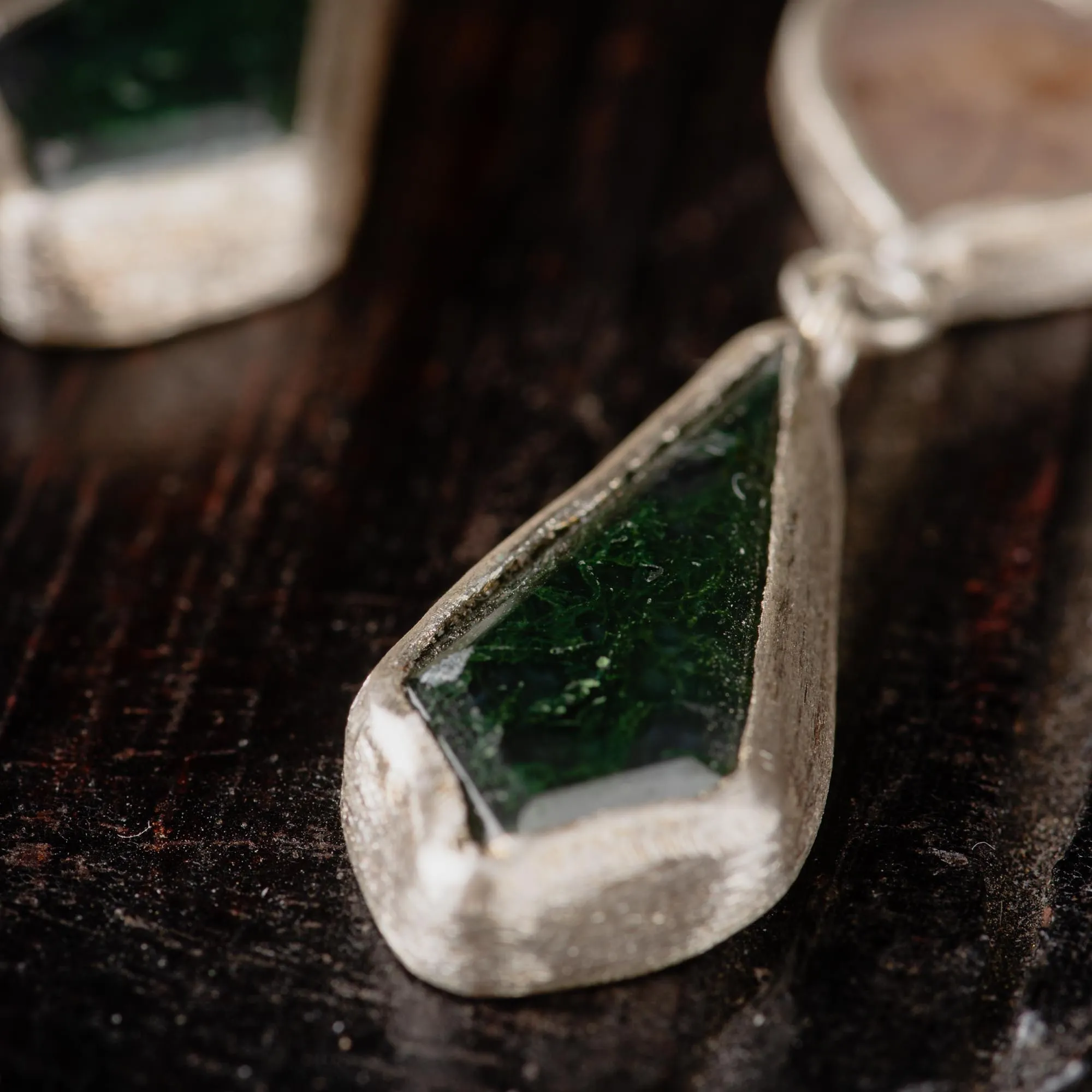 An image showing details of a sterling silver pair of earrings featuring dendritic agate in heart shaped and moss agate in kite shaped