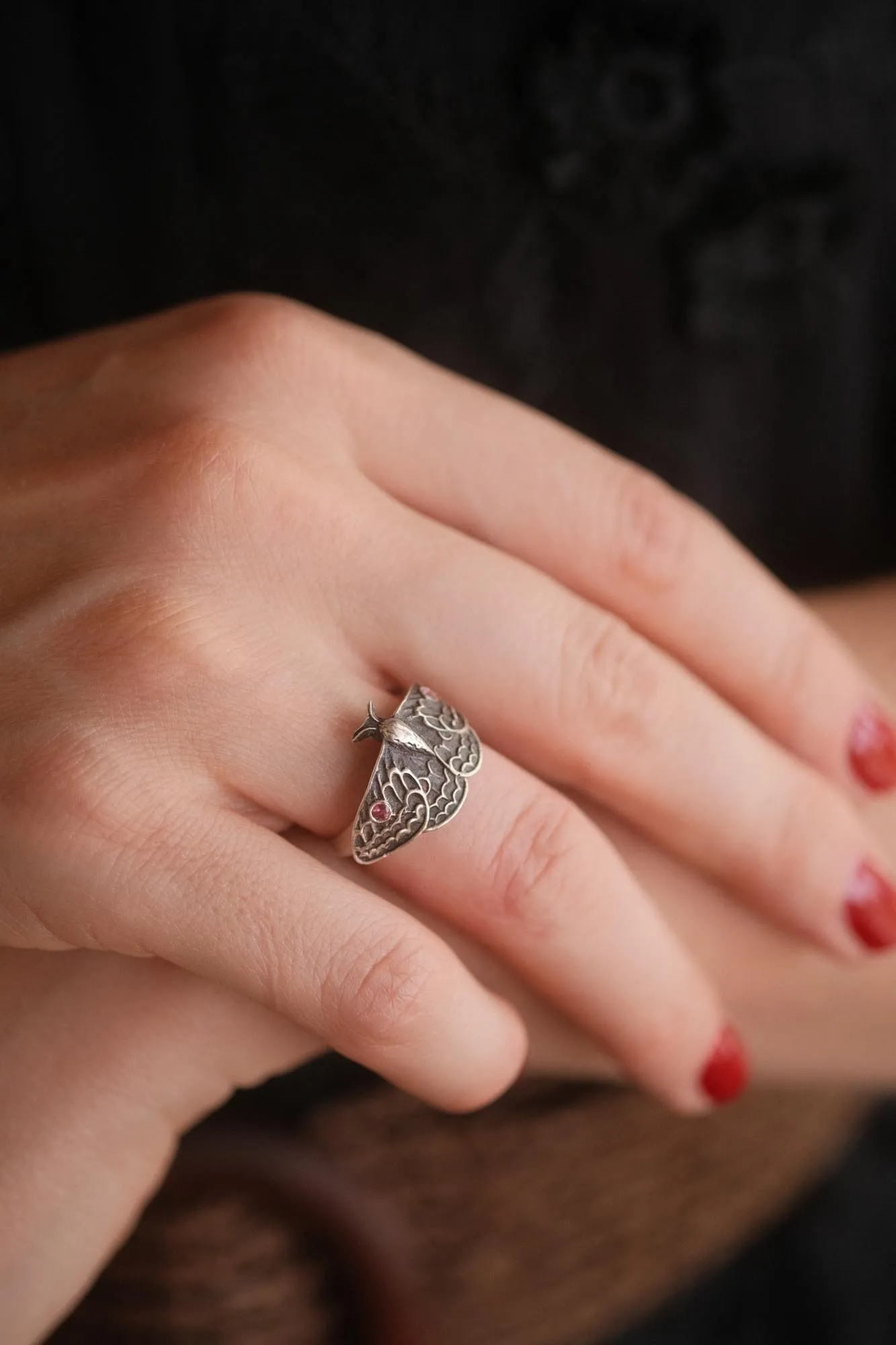 An image showing a sterling silver moth ring with two pink tourmalines on a finger