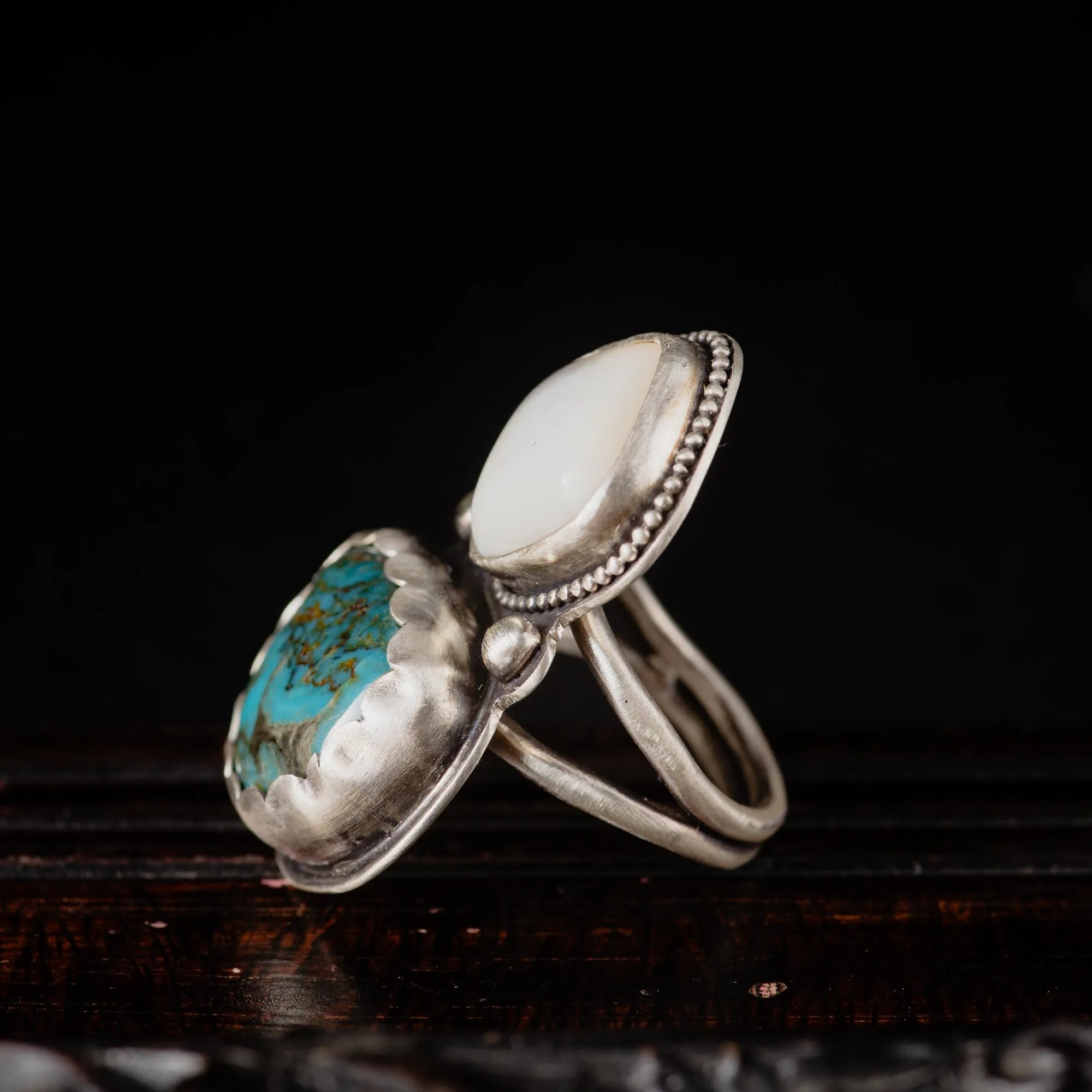 An image showing a wide ring with a combination of turquoise and mother of pearl gemstones from the side