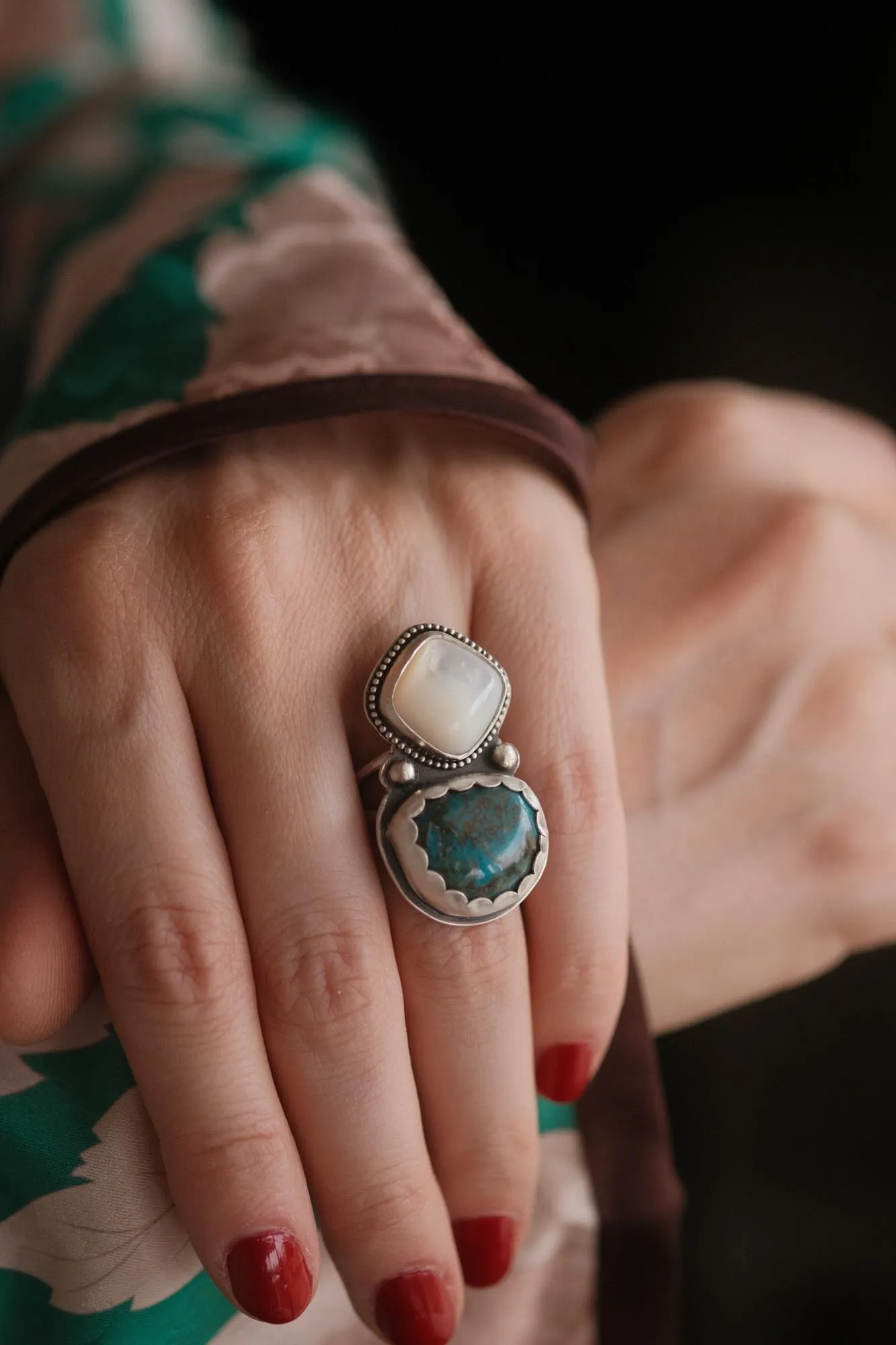 An image showing a wide ring with a combination of turquoise and mother of pearl gemstones worn on a finger