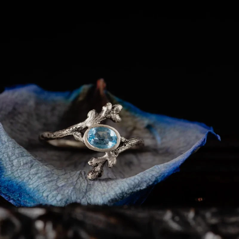 An image showing a lovely swiss blue topaz twig ring on a blue rose petal