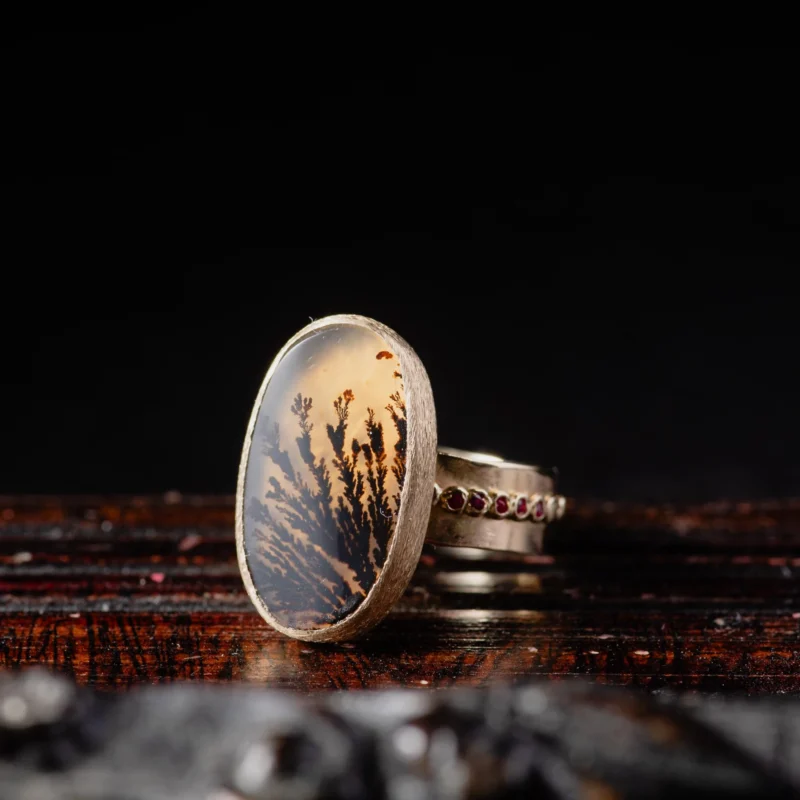 An image showing a 14k gold ring featuring an oval dendritic agate with tiny pink rubies on the sides