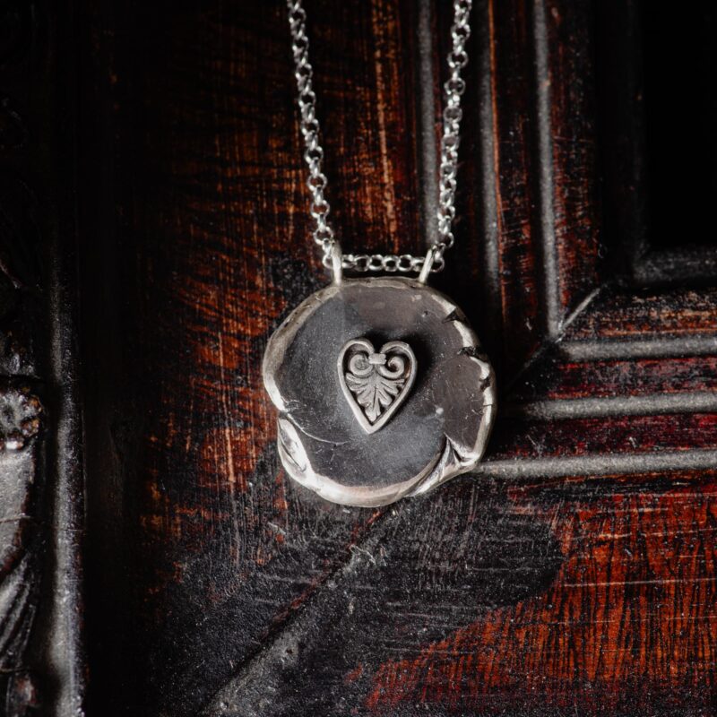 An image showing a sterling silver round organic pendant with a Greek heart motif