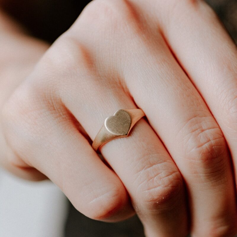 An image showing a 14K solid gold heart signet ring on a finger