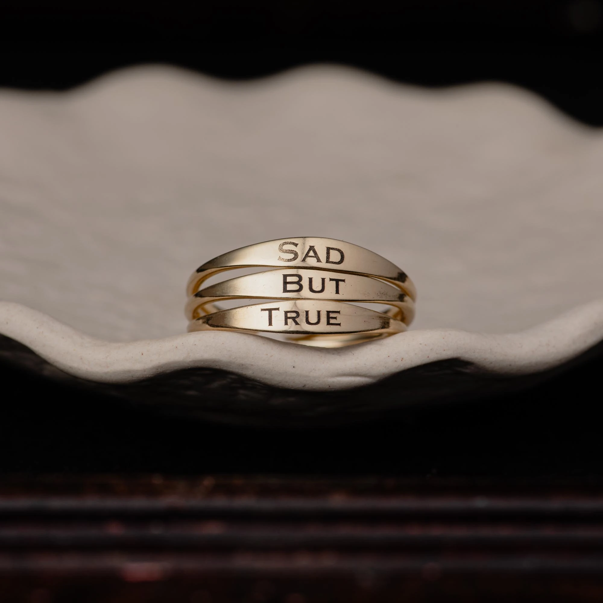 an image showing three signet rings with the words sad but true engraved