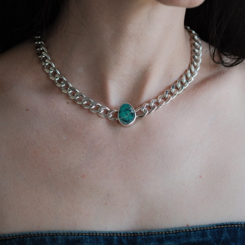 An image showing a chunky curb chain necklace with a green turquoise on a model