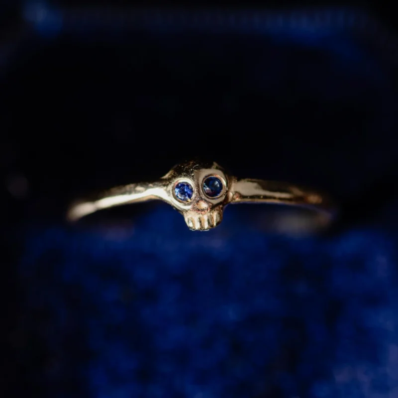 An image showing a tiny delicate 14K gold skull details with sapphire eyes