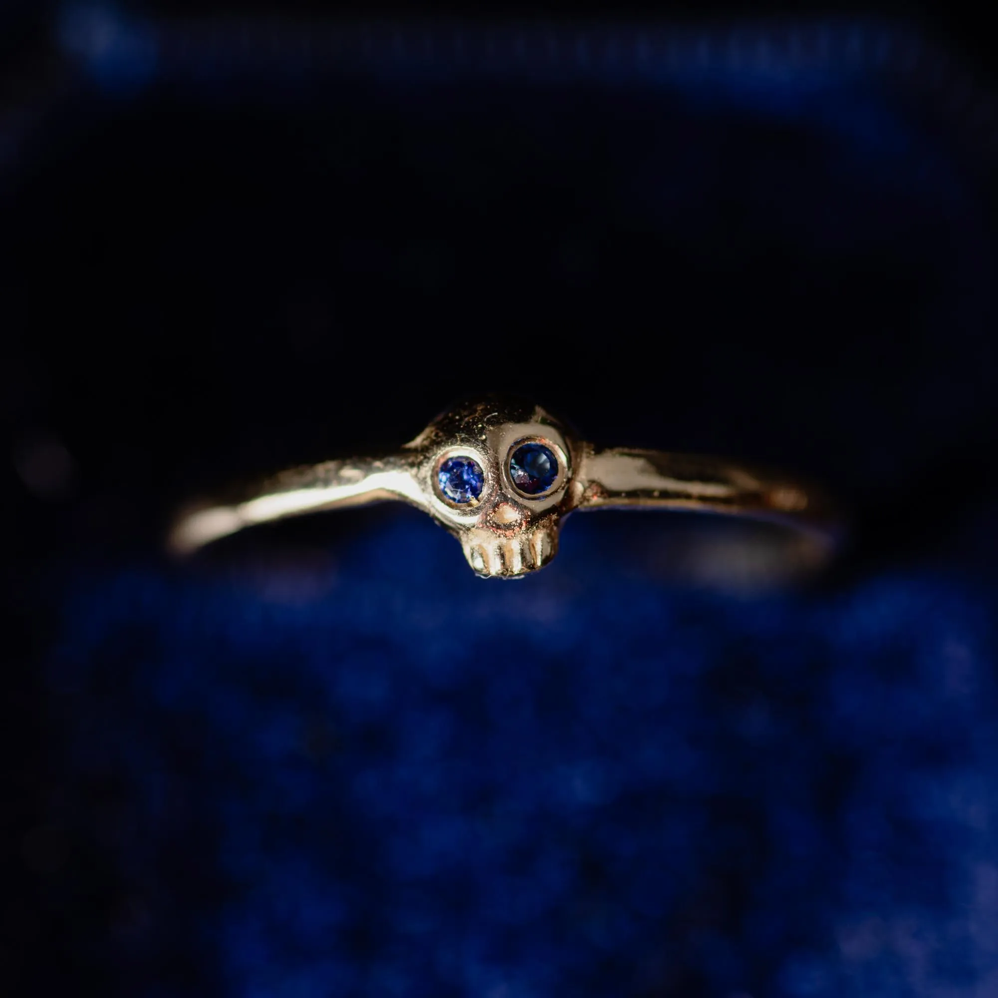 An image showing a tiny delicate 14K gold skull details with sapphire eyes
