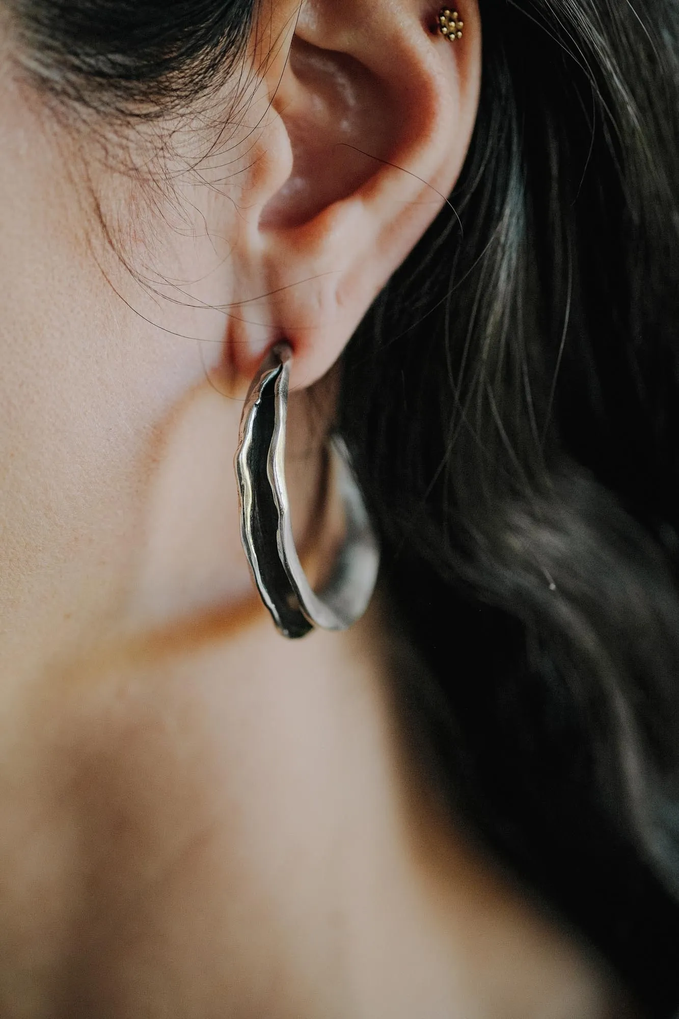 An image showing hand formed scultpural earrings on an ear